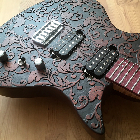 Six string electric guitar with a raised brown floral design on a black background